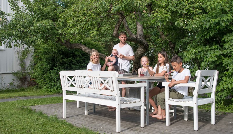 Mor og far og fire barn ved langbord i hagen
