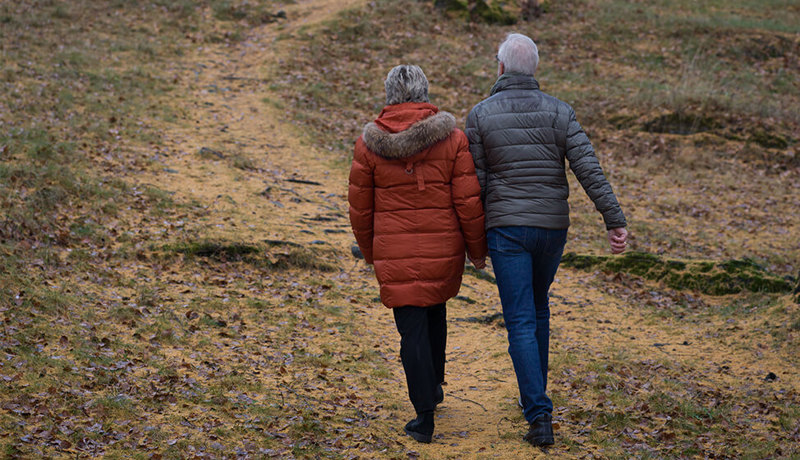 Et eldre par holder hender mens de går tur ute i skogen