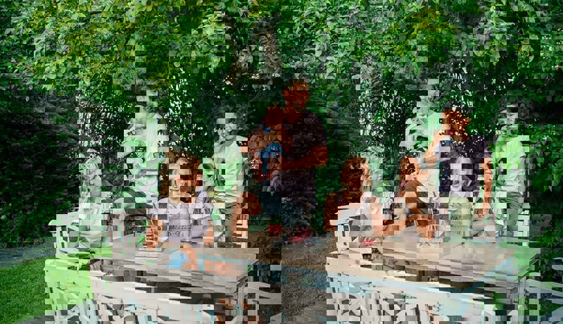 En familie med fire barn sitter ute i hagen og koser seg med saft og is