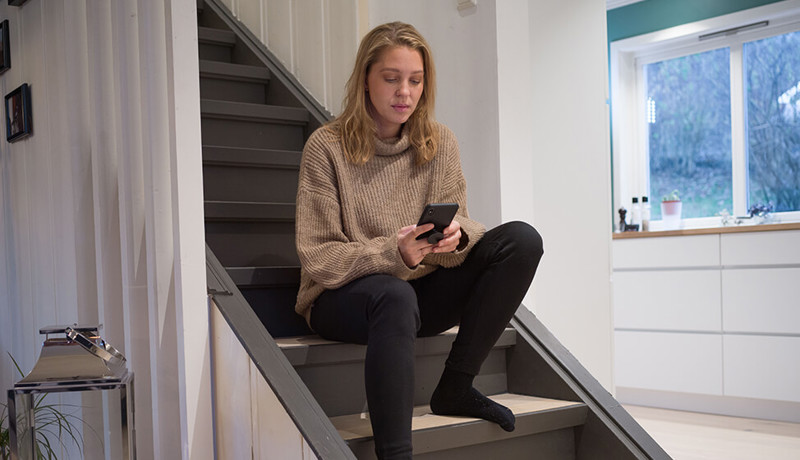 En kvinne sitter på mobilen i trappa