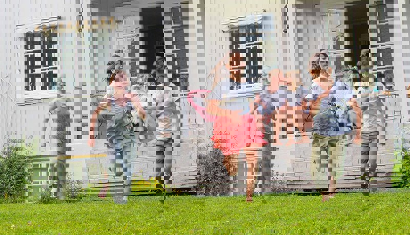 Tre barn løper ut i hagen mens foreldrene sitter på trappen