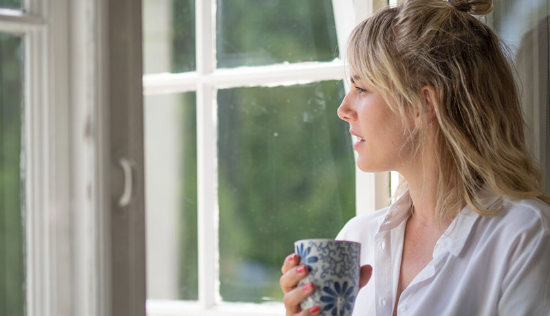 En kvinne sitter med kaffekoppen ved vinduet