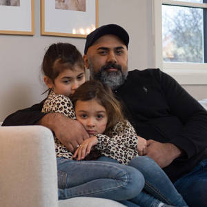 Bilde av en far med sine to døtre som sitter i sofaen