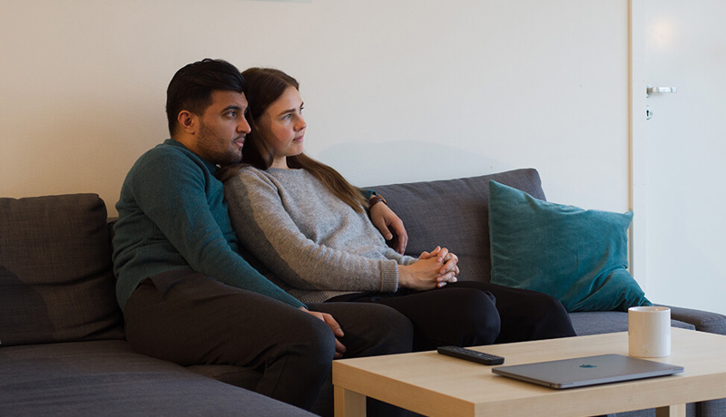 Et ungt par sitter sammen i sofaen og ser ut