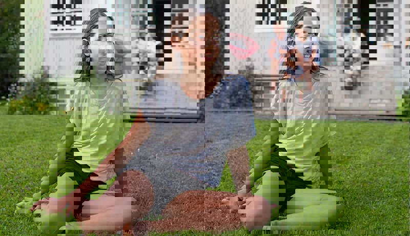 Et barn sitter på plenen mens resten av familien sitter på trappa i bakgrunnen