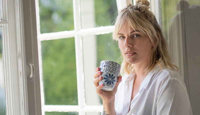En kvinne sitter med kaffekoppen ved vinduet