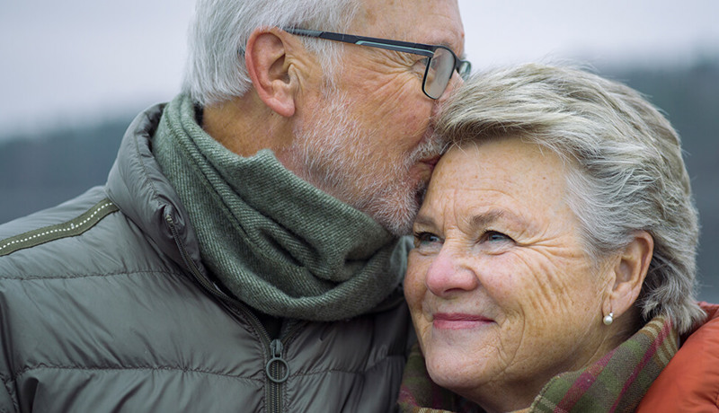 Et eldre par ser lykkelige ut når mannen kysser kvinnen på pannen