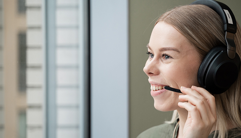 Smilende jente på kundeservice snakker med kunde i headsett. 