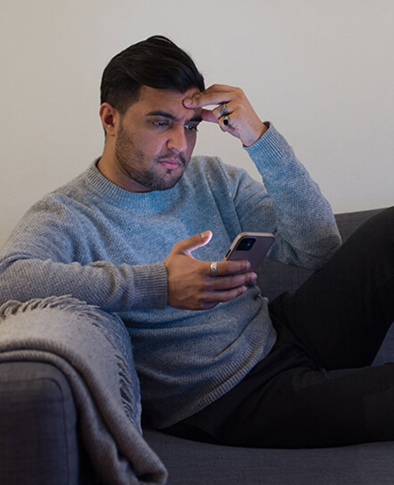 Ung mann ser på telefonen i sofaen