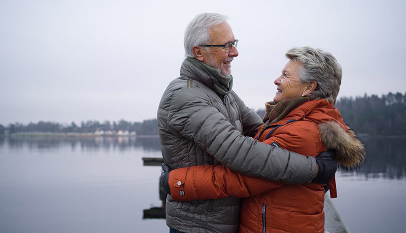 Et eldre par står ved et vann og holder rundt hverandre