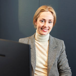 Bilde av en kvinne som sitter på kontorplassen sin og smiler