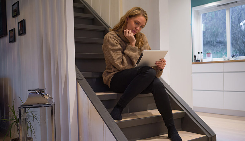 Kvinne sitter i trappa og leser på nettbrettet