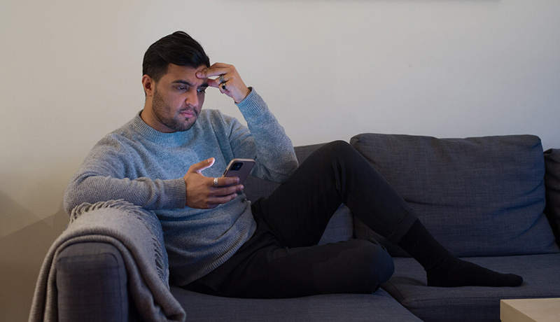 Mann sitter i sofaen og ser på telefonen
