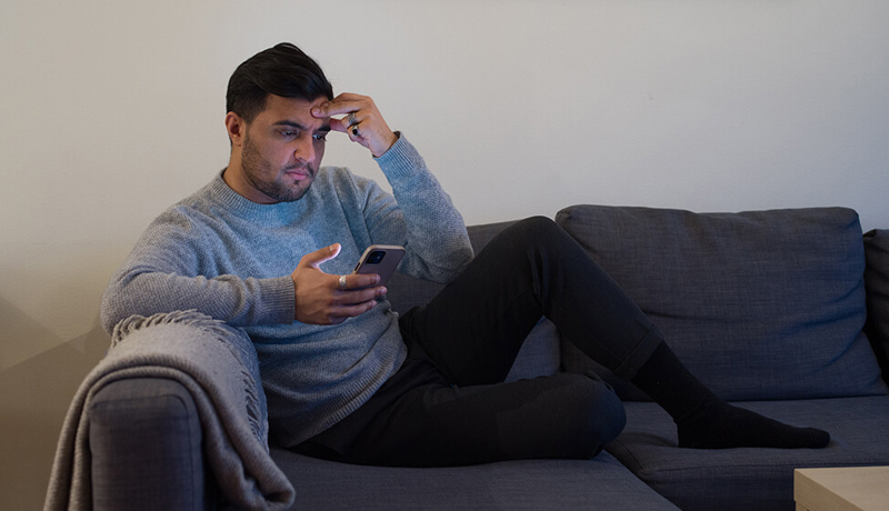 Mann sitter i sofaen og ser på telefonen