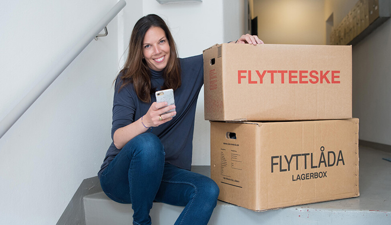 Kvinne ser på mobilen mens hun sitter med flytteesker - klar for innflytting