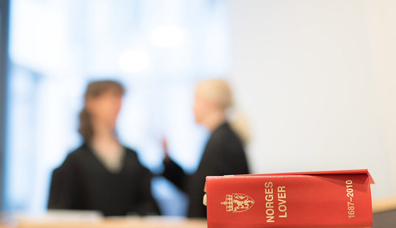 To advokater diskuterer i bakgrunnen med Norges Lover i fokus