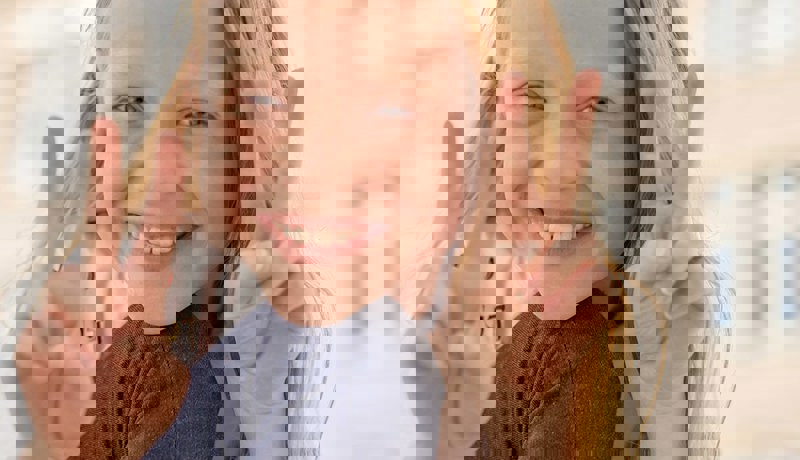 En blid unge smiler og viser "peace"-merket med begge hendende