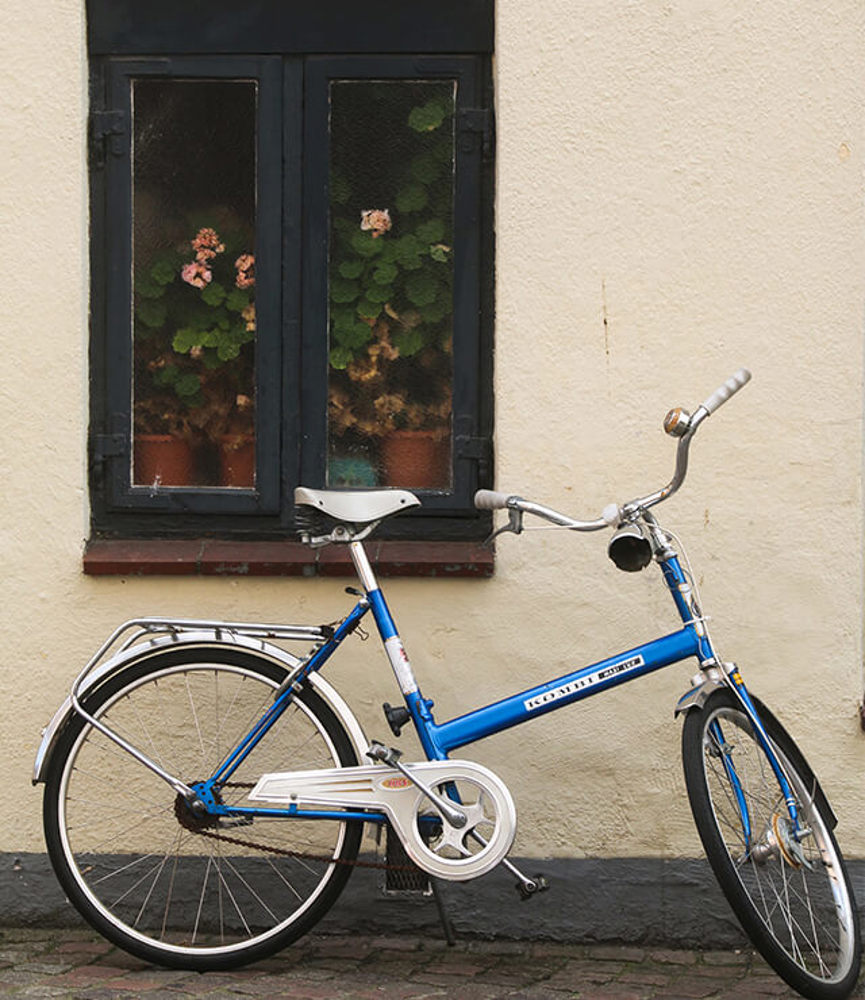Eldre sykkel står oppstilt foran en vegg og vindu