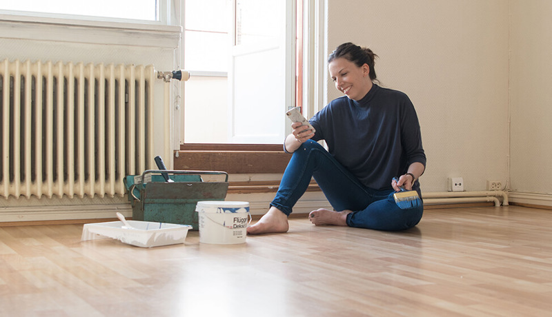Kvinne ser på telefonen og smiler mens hun maler den nye boligen sin