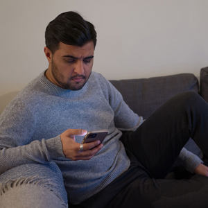 Bilde av en mann som sitter i sofaen og ser på mobilen