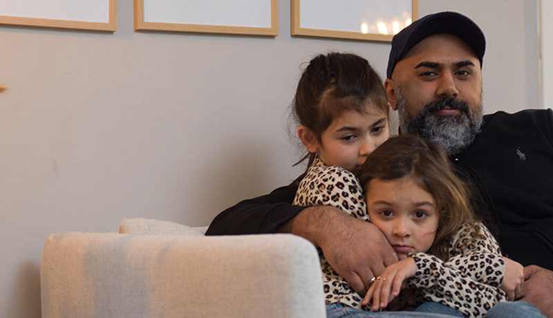 En far sitter med to barn i sofaen