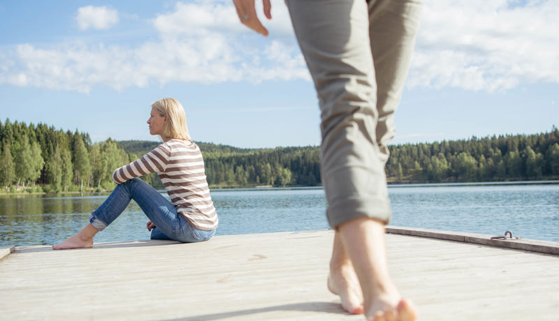 Kvinne sitter på en brygge, mann går fra henne