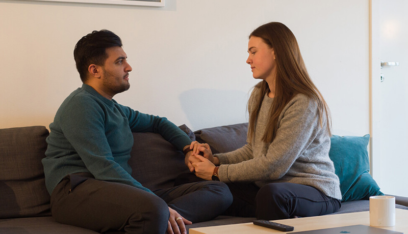 Et ungt par sitter i sofaen og holder hender