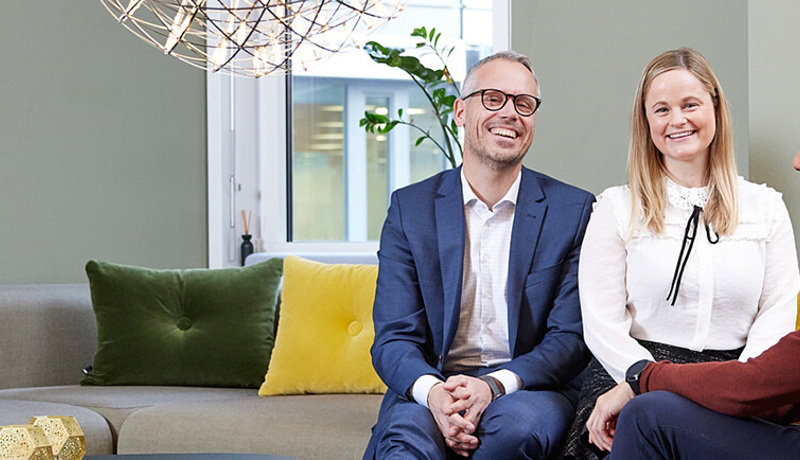 Bilde av tre personer som har det hyggelig og smiler i sofaen