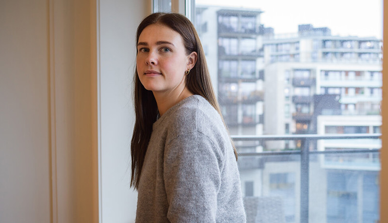 En ung kvinne ser spørrende ut mens hun sitter i hjemmet sitt