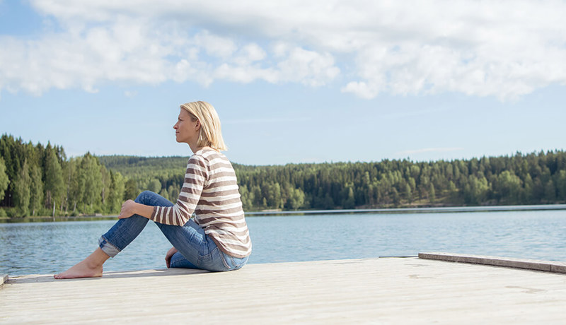Ung kvinne sitter på brygga og ser utover