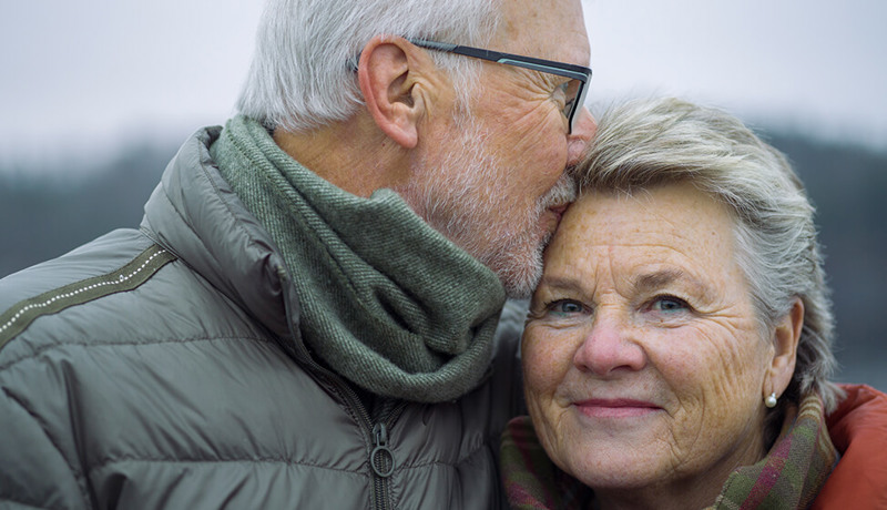Et eldre par ser lykkelige ut når mannen kysser kvinnen på pannen